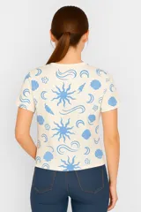 Remera amarilla con estampado de motivos playeros en blanco: soles, olas y conchas marinas.