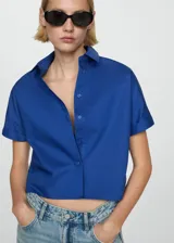 Camisa crop blanca con cuello camisero y manga corta, confeccionada en 100% algodón.