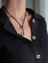 Gargantilla marrón de cuero con dije de bronce en forma de letra M.