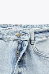 Pantalón de jean color crudo, de tiro alto, corte recto y largo tobillero. Tiene cinco bolsillos, cierre frontal con cremallera y botón metálico.
