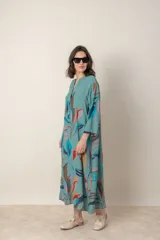 Vestido largo de lino color verde militar con estampado de hojas en tonos azul, naranja y marrón. Tiene cuello mao con botones, mangas tres cuartos y un bolsillo en el pecho.