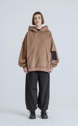 Buzo hoodie marrón de corte oversize, confeccionado en algodón rústico. Tiene capucha forrada, bolsillo tipo bomber con cierre en la manga y bolsillo canguro.