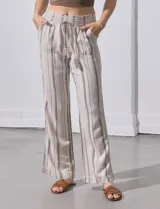 Pantalón de lino color beige con rayas verticales marrones, pretina ancha con punto smock y lazo ajustable, bolsillos verticales delanteros y bolsillos aplicados traseros.