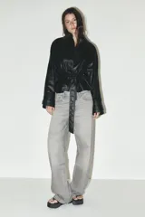 Cazadora negra de efecto piel, con cuello solapa, manga larga, bolsillos de vivo en delantero, cinturón en mismo tejido y cierre frontal con botones.