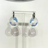 Aros colgantes con forma irregular que simulan una oreja de mar, con detalles iridiscentes en tonos azules y blancos. Los aros son de acero quirúrgico hipoalergénico.