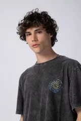 Remera de hombre color gris oscuro con efecto gastado (snow wash), corte semi-oversize y un pequeño estampado circular en el pecho que simula una obra de arte.