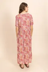 Vestido largo color ladrillo con estampado de hojas en tonos blanco y amarillo. Tiene escote en V, mangas cortas y botones frontales.