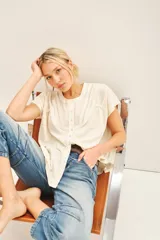 Camisa color crema de manga corta, con combinación de tejido de punto y plano, detalles de volados y frunces en pechera y espalda, y acceso con botones nacarados.