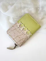 Billetera pequeña de cuero con cierre metálico, diseño color block en verde lima y beige con detalle de cordones cruzados.