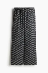 Pantalón recto de viscosa color negro con estampado de flores pequeñas en blanco. Tiene tiro bajo, elástico en la cintura y bolsillos al bies.