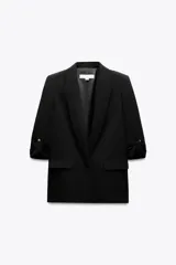 Blazer negro abierta con cuello solapa y hombreras. Manga por debajo del codo acabada en vuelta con trabilla y botón dorado. Bolsillos delanteros con solapa.
