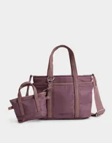 Cartera tipo city de tela deportiva color lila, con doble asa corta y correa larga regulable y desmontable. Incluye un pouch lateral con forma de bolso.
