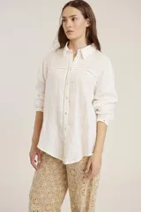 Camisa blanca de manga larga, corte holgado, con cuello camisero y detalles de bordados perforados (calado) verticales en el frente.