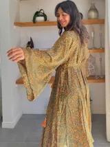 Kimono largo de seda con estampado floral en tonos verde, marrón y beige. Tiene mangas amplias y corte cruzado con lazo ajustable en la cintura.