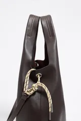 Bolso de mano tipo shopper de cuero color marrón oscuro, con estructura blanda y asa extraíble. Incluye logo metálico de la marca Bimba y Lola, acabados metálicos, bolsillo interior e interior con etiqueta de tejido.