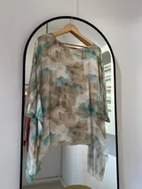 Blusa de seda italiana con estampado abstracto en tonos aqua, marrón y blanco. Tiene cuello redondo y corte asimétrico en el ruedo. Incluye musculosa interior.