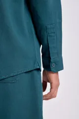Camisa de manga larga color verde azulado, con cuello camisero, botones frontales y dos bolsillos de parche con tapa en el pecho.