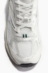Championes deportivos blancos con detalles en verde y plateado, de malla y tejido revestido, con cierre de cordones y suela gruesa con diseño.
