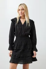 Vestido corto negro con escote en V, mangas largas abullonadas con puños elásticos, falda con volados y cinturón trenzado.