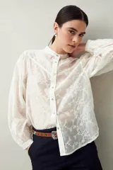 Camisa blanca con bordado floral en contraste, cuello mao, abotonadura frontal y mangas largas con frunces en los hombros.