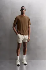 Camiseta deportiva marrón confeccionada en tejido técnico ligero y elástico con estructura perforada. Cuello redondo, manga corta y bajo asimétrico con aberturas laterales. Detalle de logo estampado.