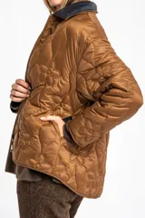 Campera capitoneada de color marrón con diseño de flores pespunteadas, cuello camisero en contraste oscuro y cierre frontal de cremallera.