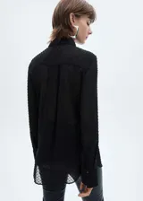 Camisa negra de plumeti con cuello camisero, manga larga con puños abotonados y cierre frontal de botones oculto.