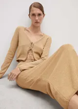 Cárdigan color beige de tejido de punto grueso, con cuello pico, diseño crop, corte recto, cierre de lazo en la parte delantera y manga larga.