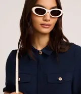 Camisa color beige de tela airflow, con cuello camisero, mangas cortas con detalle de pliegue, bolsillos con solapa en el pecho y cierre frontal con botones metalizados.