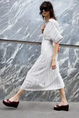 Vestido midi de rayas verticales color beige y negro, con cuello solapa, escote pico, manga corta y cierre frontal con botones.