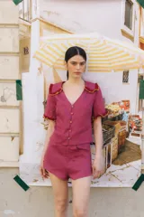 Blusa de lino color fucsia, con cuello tipo bebé y manga corta. Presenta detalles de crochet en color rojo y amarillo en el cuello y los puños. Tiene cierre frontal de botones.