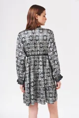 Vestido corto con estampado abstracto en tonos celeste, negro y blanco. Tiene escote en V con ribete de terciopelo negro, mangas largas con puños fruncidos y corte escalonado en la falda.