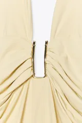 Vestido midi color crema de poliamida con cuello halter con lazada, escote pico pronunciado, detalle de pieza metálica y tejido con frunces.