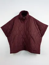 Poncho acolchado color mostaza con cuello alto y abertura frontal con cierre. Presenta un patrón capitoné de formas ovaladas y bolsillos delanteros.