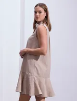 Vestido corto blanco sin mangas, con cuello camisero, abotonadura frontal parcial y ruedo con volantes.