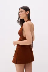 Top halter de cuero color beige, con escote profundo en V y cierre frontal con tiras horizontales.