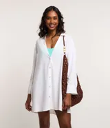 Salida de playa tipo camisa blanca de viscolino con cuello inglés, mangas largas, cierre por botones y aberturas laterales.