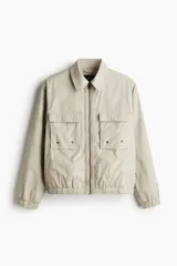 Campera color beige de corte holgado, con cuello camisero, cierre frontal y bolsillos superiores con solapa.