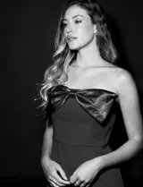 Vestido de fiesta corto strapless, color negro, confeccionado en crepe. Presenta escote recto con aplique de moño en satén y tajo en la parte delantera.