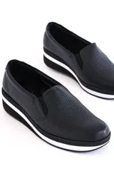 Zapatillas slip-on de cuero negro con plataforma blanca y elástico en los laterales.