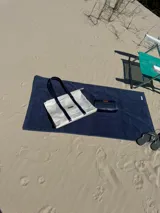 Bolso de lona color blanco con asas de cuero azul marino y etiqueta de cuero con el logo de la marca.