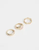 Set de tres anillos dorados de metal: uno liso, uno con eslabones calados y uno con diseño de sello con moño esmaltado.