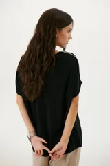 Remera negra de corte holgado con cuello redondo y mangas cortas con dobladillo. Presenta una línea diagonal blanca que cruza el frente desde el hombro hasta la cadera.