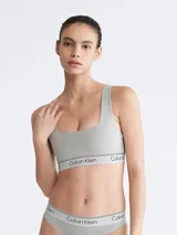 Corpiño deportivo Calvin Klein color gris, sin relleno, con escote en U, espalda cruzada y banda elástica con logo.