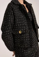 Chaqueta corta de tweed negro con detalles en blanco, cierre frontal con cremallera dorada y cuello clásico.