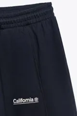 Pantalón jogger azul marino de tiro alto con cintura elástica ajustable, bolsillos delanteros, texto blanco estampado en la pierna izquierda y puños elásticos en los tobillos.