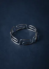 Brazalete rígido de acero quirúrgico plateado con diseño calado de guarda griega.