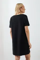 Vestido corto negro con flecos en el pecho y tachas plateadas en los hombros.