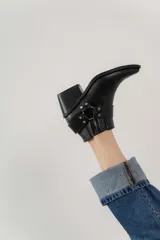 Botas cortas de cuero negro con puntera fina, caña baja con elásticos laterales y hebilla decorativa.