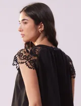 Blusa negra de crepe con apliques de crochet en los hombros. Tiene cuello redondo, mangas cortas y espalda con abertura ojal y botones.